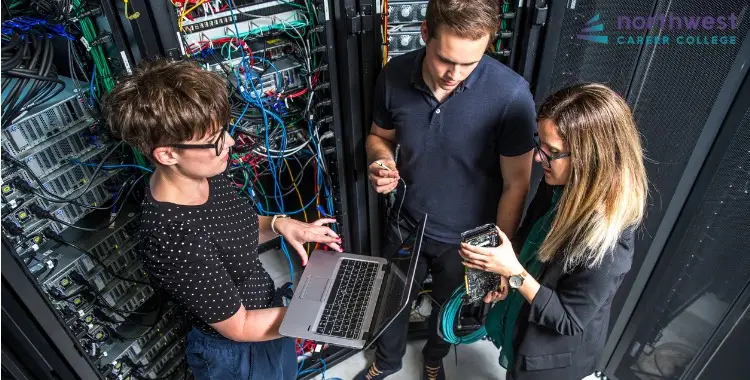 Three individuals troubleshoot network connectivity issues near server racks, discussing solutions with a laptop in hand.