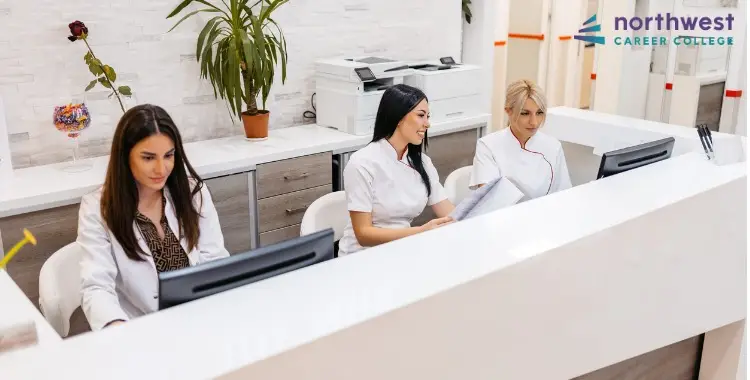 Three women in dental attire at a front desk, engaged in tasks, showcasing the Dental Front Desk Experience.