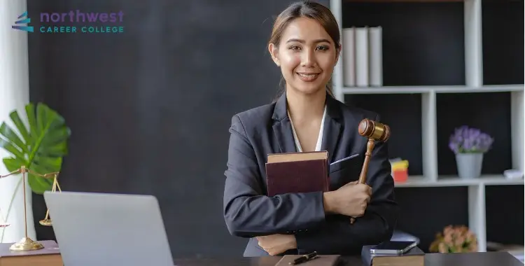 A confident woman in a suit holds a gavel and books, representing What Does a Corporate Legal Assistant Do.