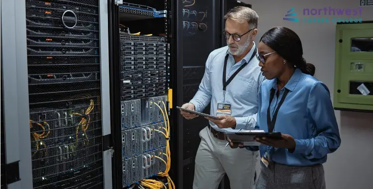 An IT Specialist and an IT Technician examine server equipment in a data center, discussing their findings.