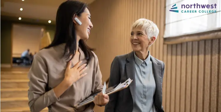 Two women engage in a friendly conversation, possibly discussing roles like Business Administration Assistant, in a modern.