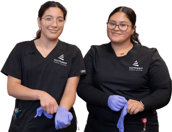 Two students at phlebotomy school Las Vegas prepare to put on gloves, smiling and dressed in black scrubs.