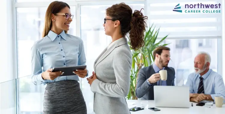 Two women discuss a tablet in a modern office, highlighting Best Practices in Effective Project Management for Business.