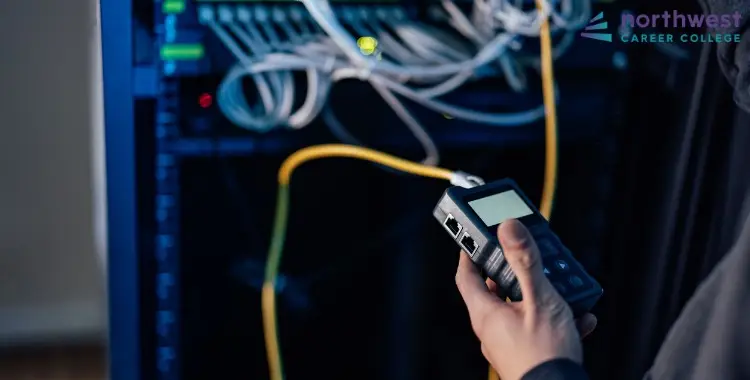 A technician uses a network tester near cables and equipment, illustrating Which Tools Are Typically Used by the IT.