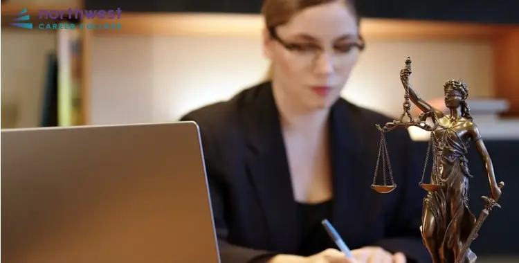 A woman in a suit writes at a desk with a laptop and a statue of Lady Justice, symbolizing Becoming a Legal Assistant.