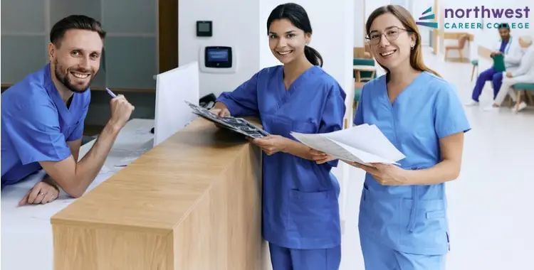 Three medical administrative assistants in scrubs smile at the reception desk, embodying Customer Service Tips for Medical.