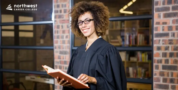 A smiling woman in a judges robe holds a book, illustrating What Is a Paralegal Not Allowed to Do in legal settings.