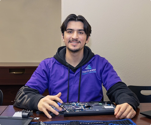 A student in a purple shirt smiles while working on a laptop, showcasing skills learned in IT technician classes.