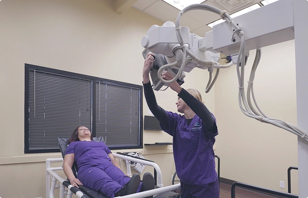 A technician adjusts an X-ray machine above a patient in a clinical setting, showcasing skills learned in xray school.