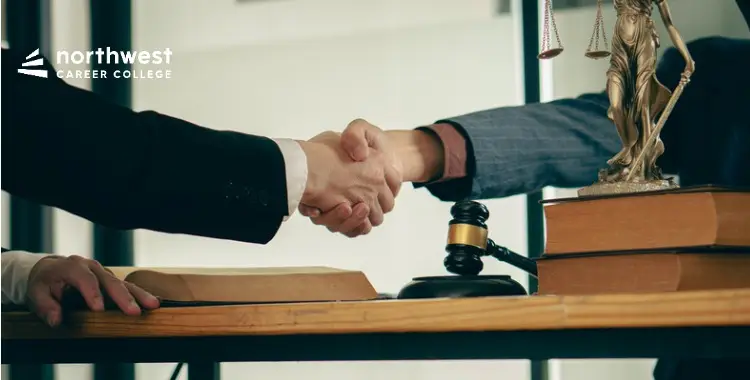 Two professionals shake hands over a desk with legal books and a gavel, highlighting the benefits of working as a legal.